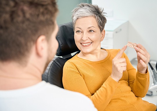 A woman pointing to a denture while talking to her dentist