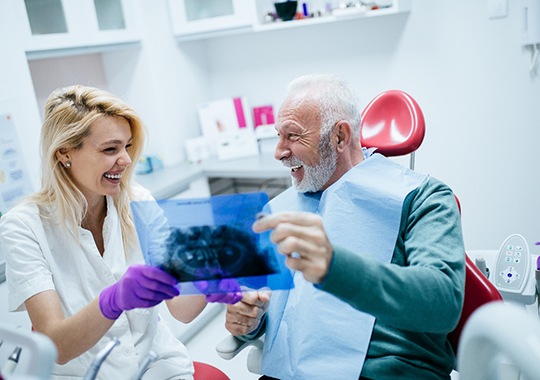An older, smiling man pointing at a dental X-ray
