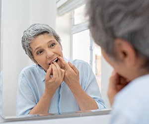 An older woman flossing in front of a bathroom mirror