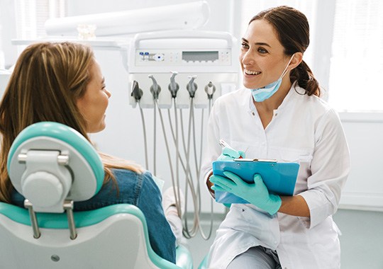 Smiling dentist with clipboard talking to patient in treatment room